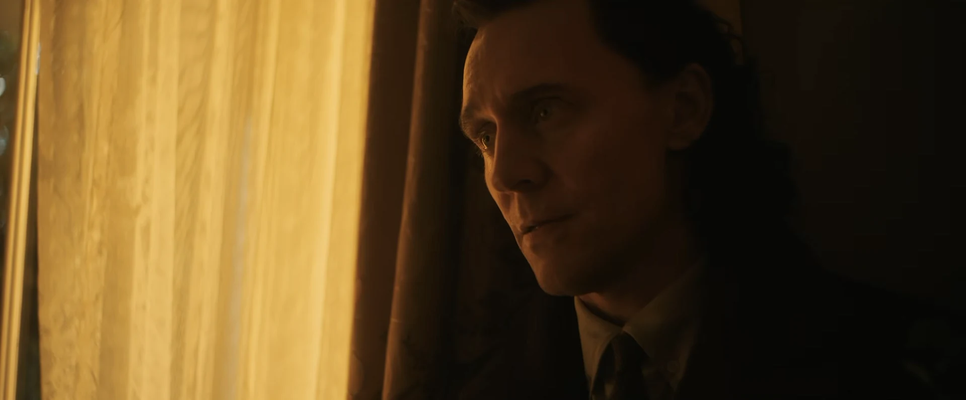 Loki mirando por una ventana iluminada por luz cálida, con gesto pensativo, en el tráiler de Avengers: Doomsday